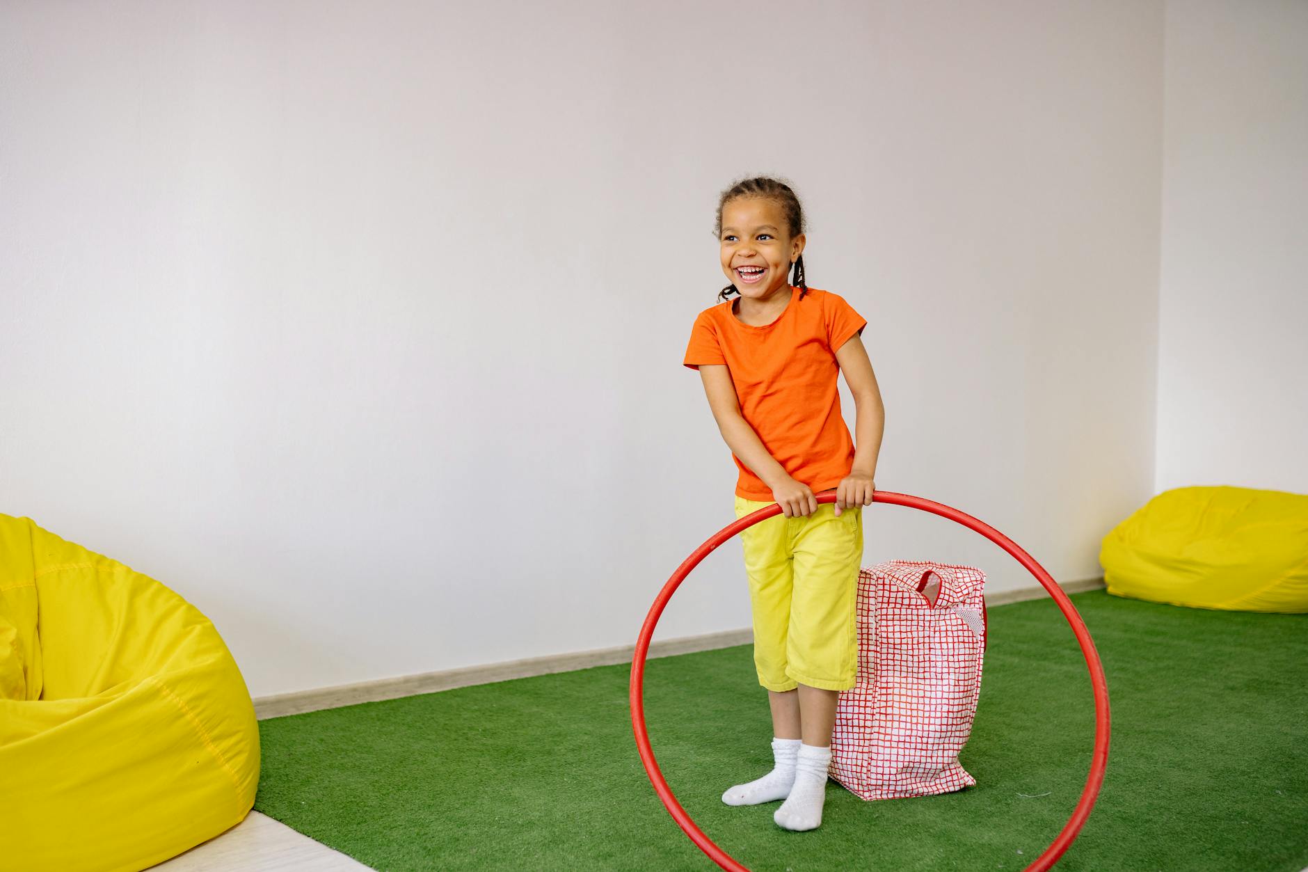 Dziewczynka bawi się obręczą w pokoju, w tle kolorowe pufy sako