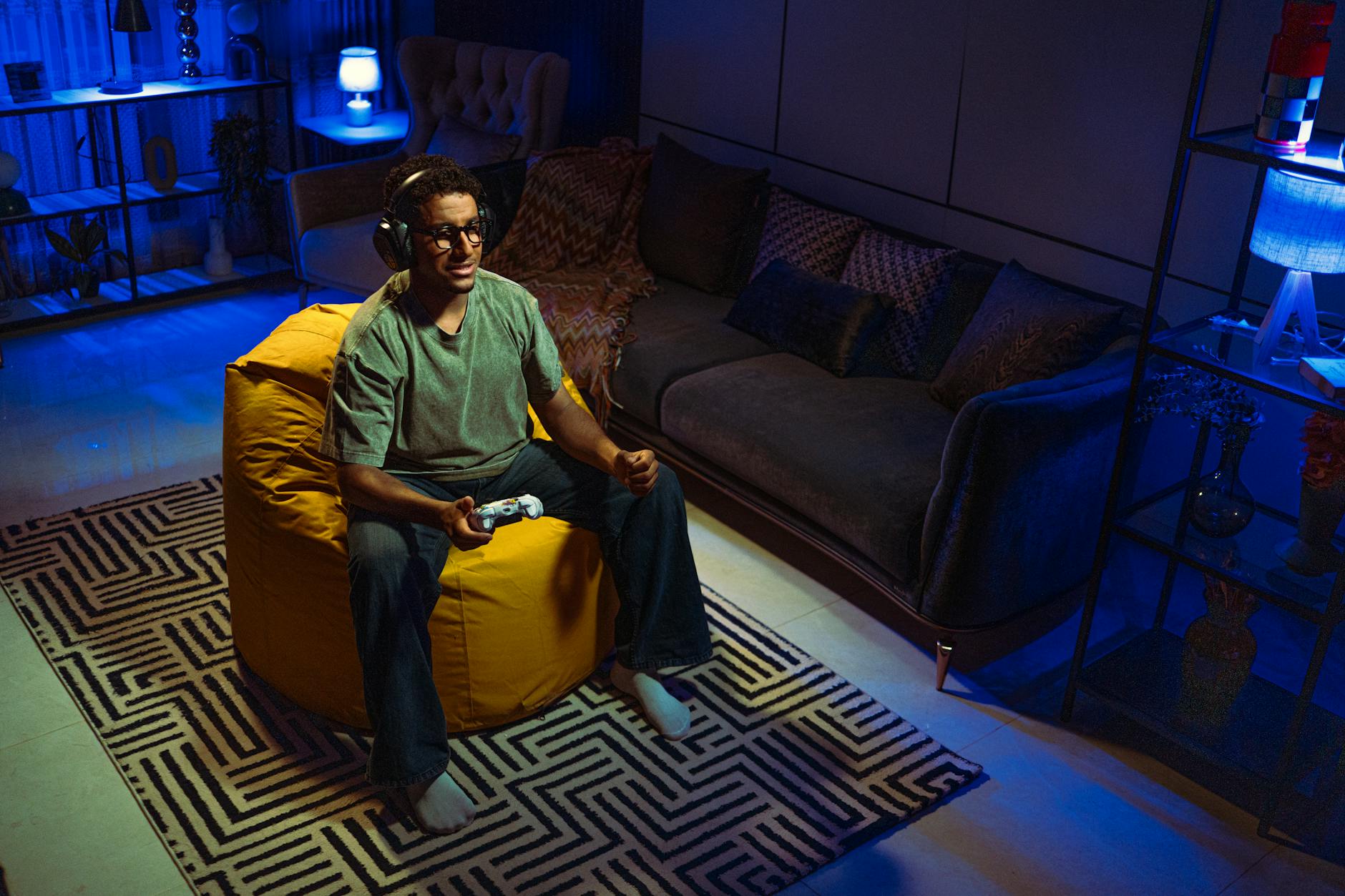Gracz siedzi na pufie sako i gra na konsoli w przyciemnionym salonie