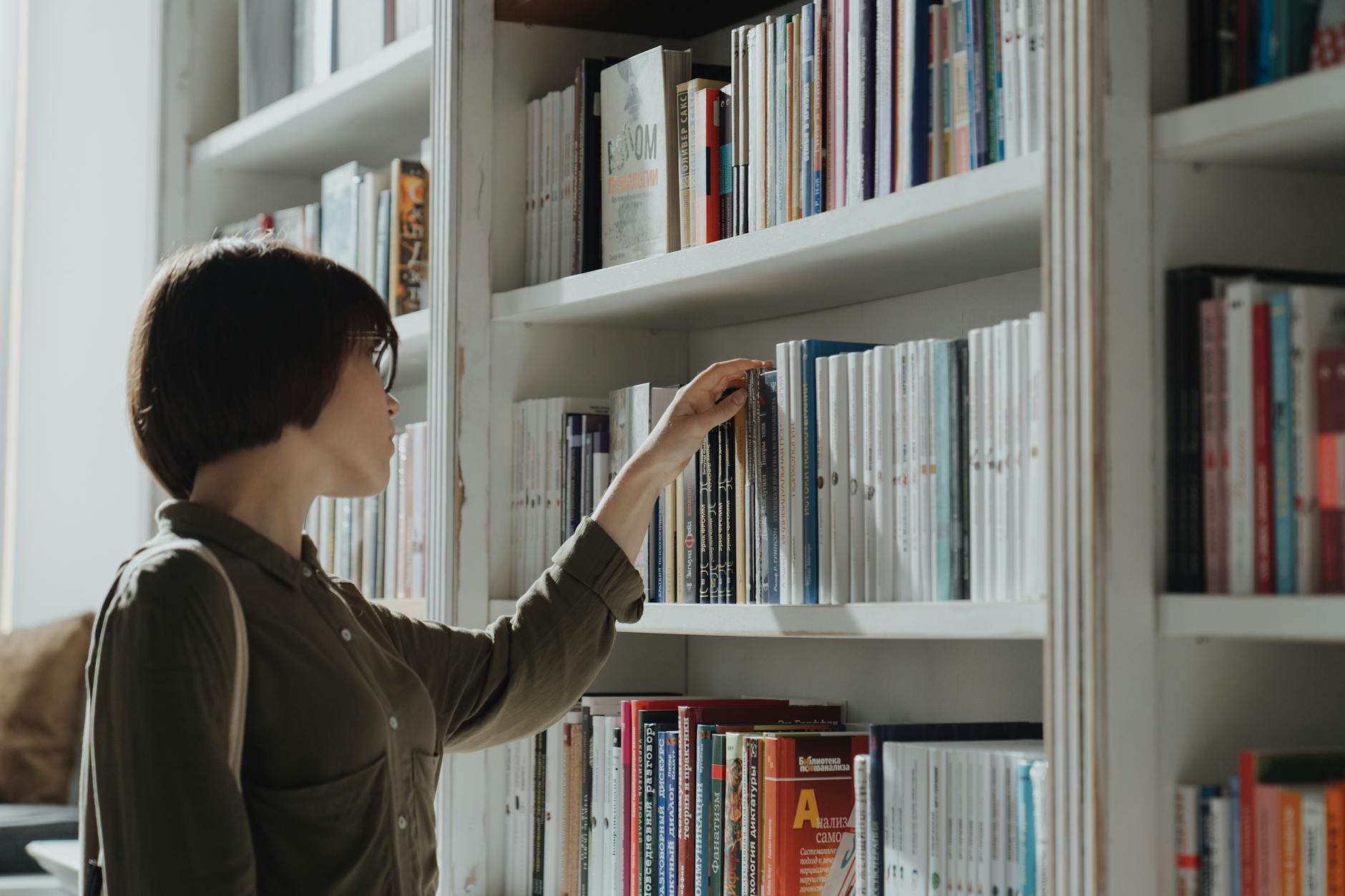 Kobieta przegląda książki na regale w nowoczesnej bibliotece