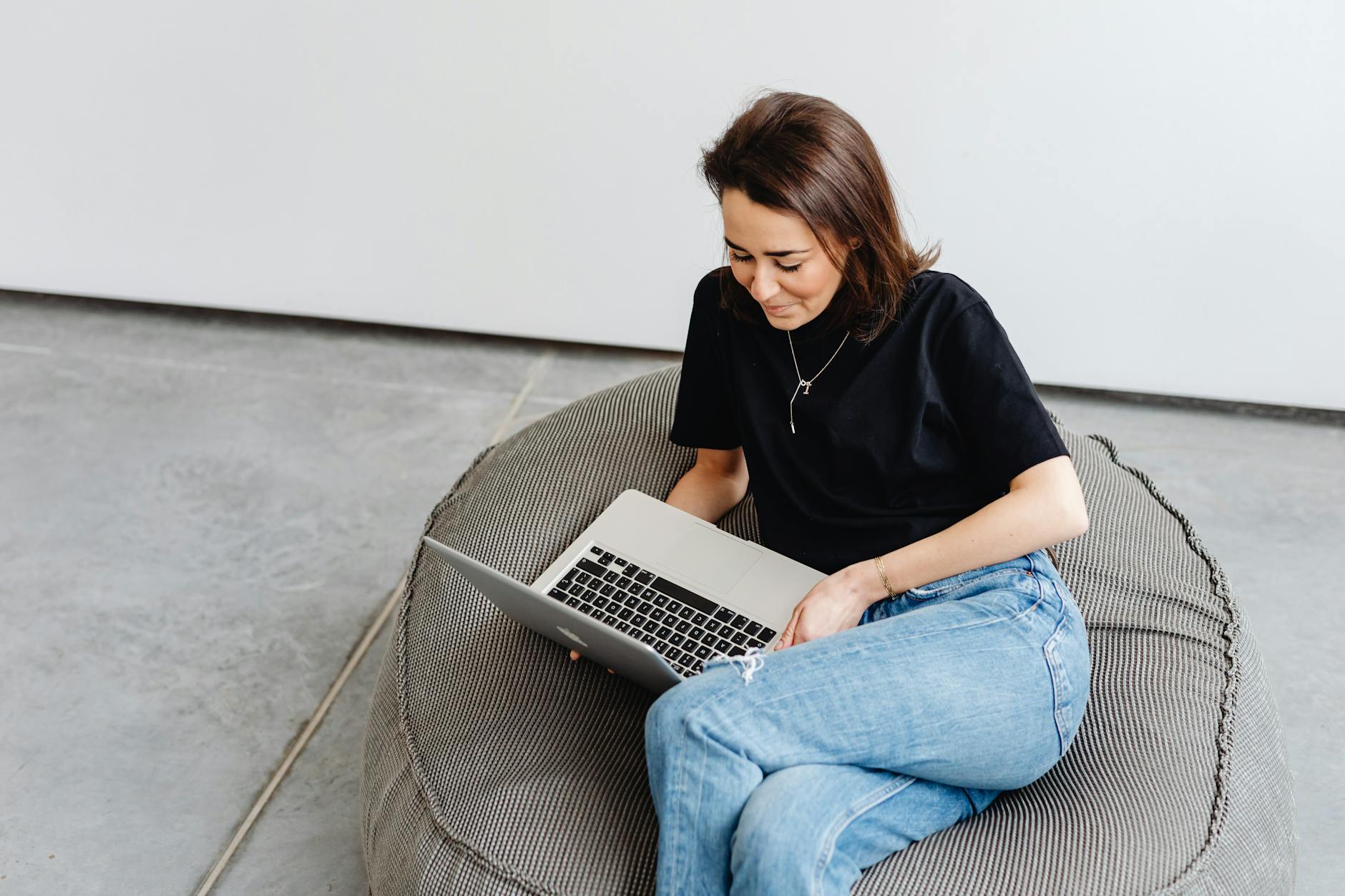 Kobieta w casualowym stroju siedzi na pufie sako z laptopem