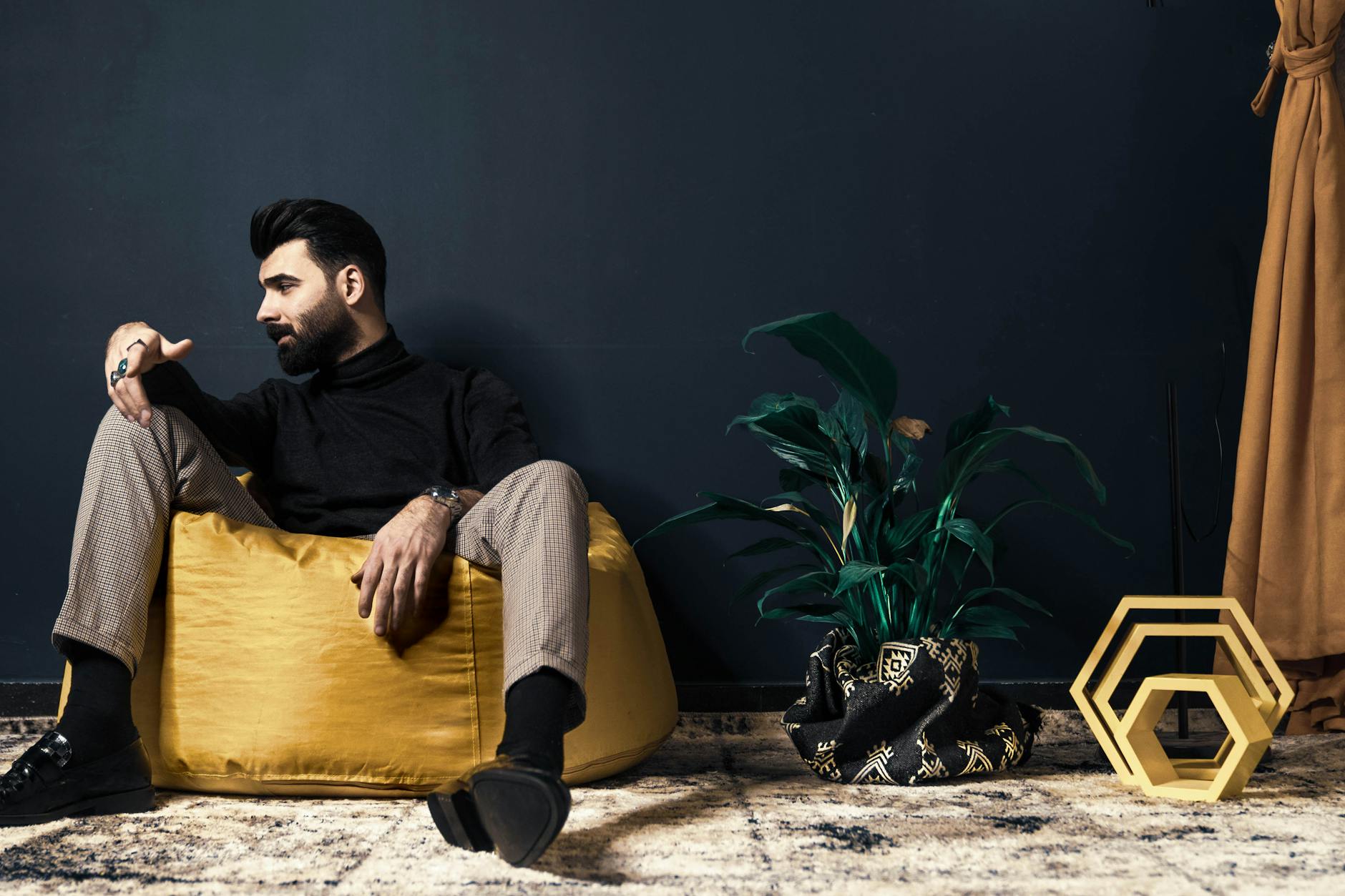 Mężczyzna z brodą siedzi na żółtej pufie sako w nowoczesnym salonie