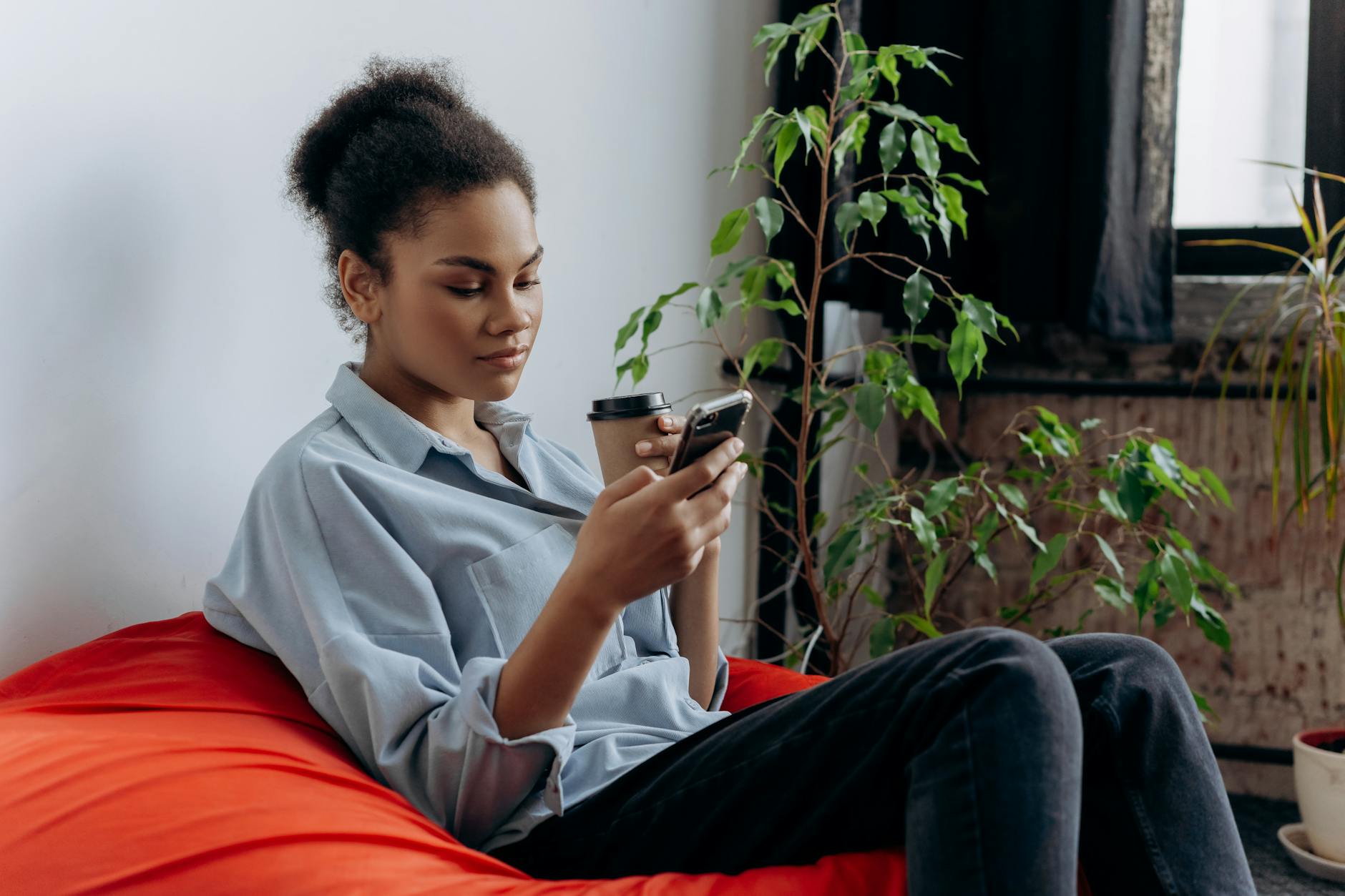 Kobieta przy małym biurku z telefonem i kawą, otoczona roślinami
