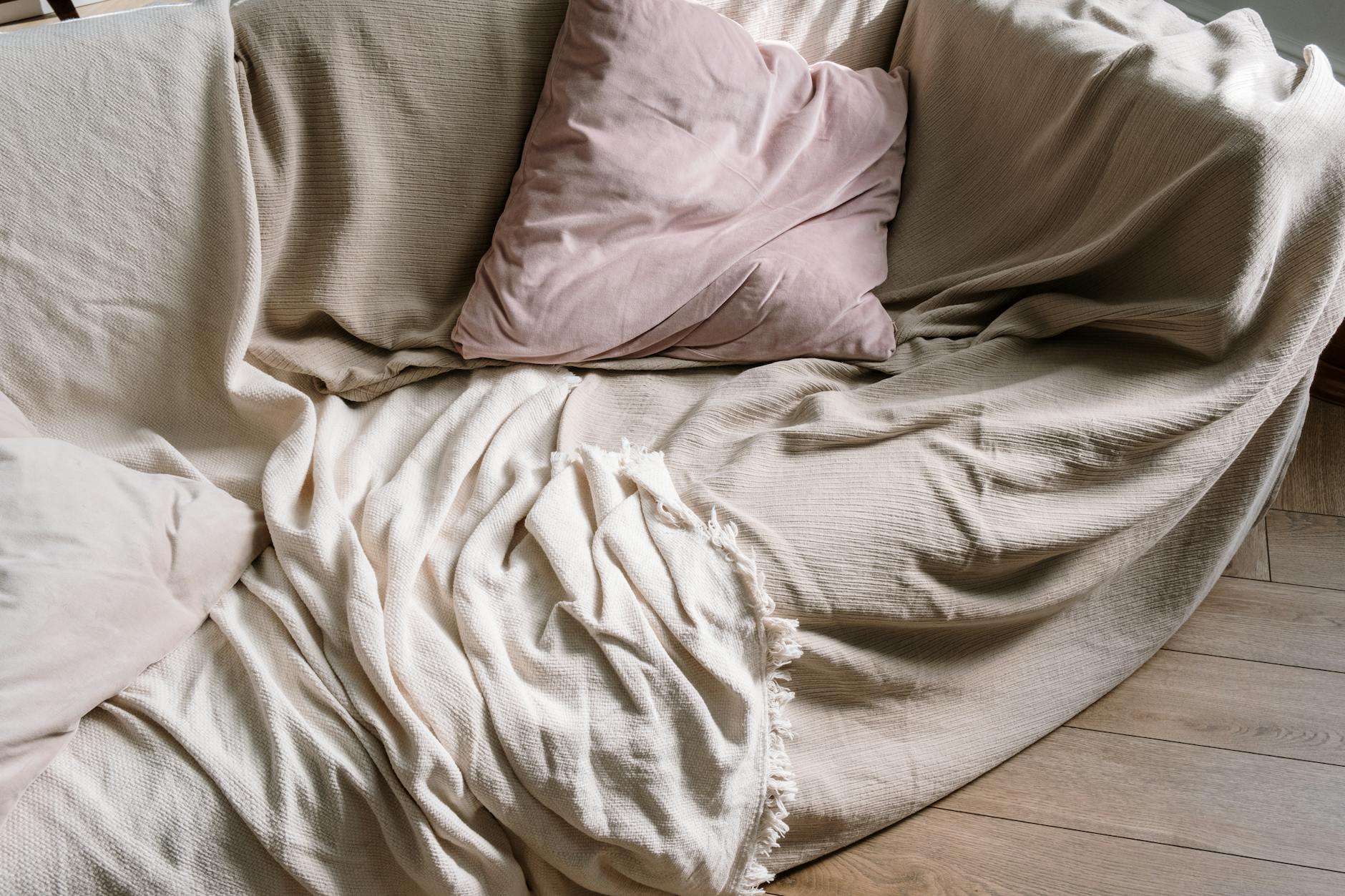 Beżowa sofa z poduszkami i kocem stojąca na drewnianej podłodze