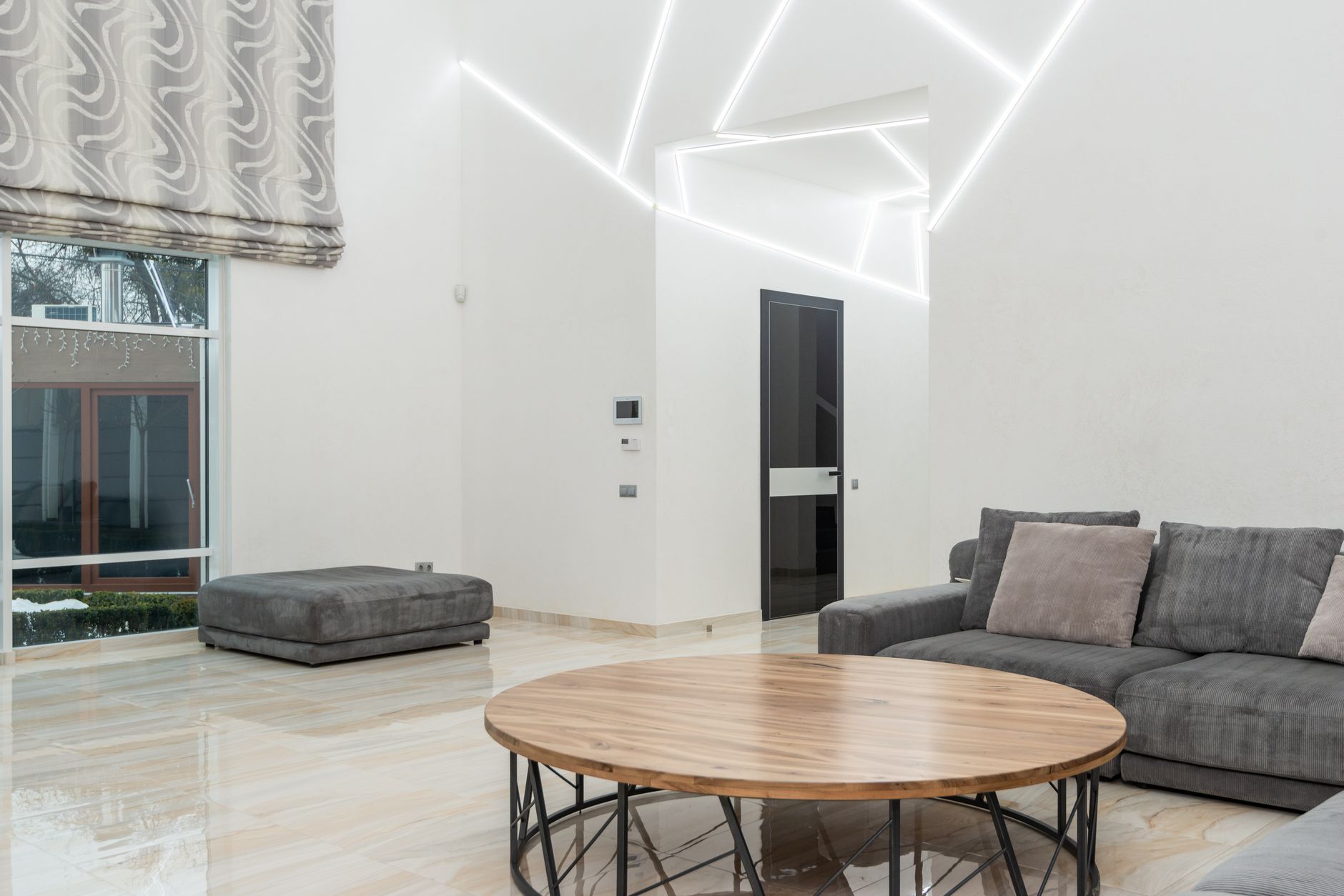 Jasny minimalistyczny salon z sofą, stołem i pufą przy dużym oknie
