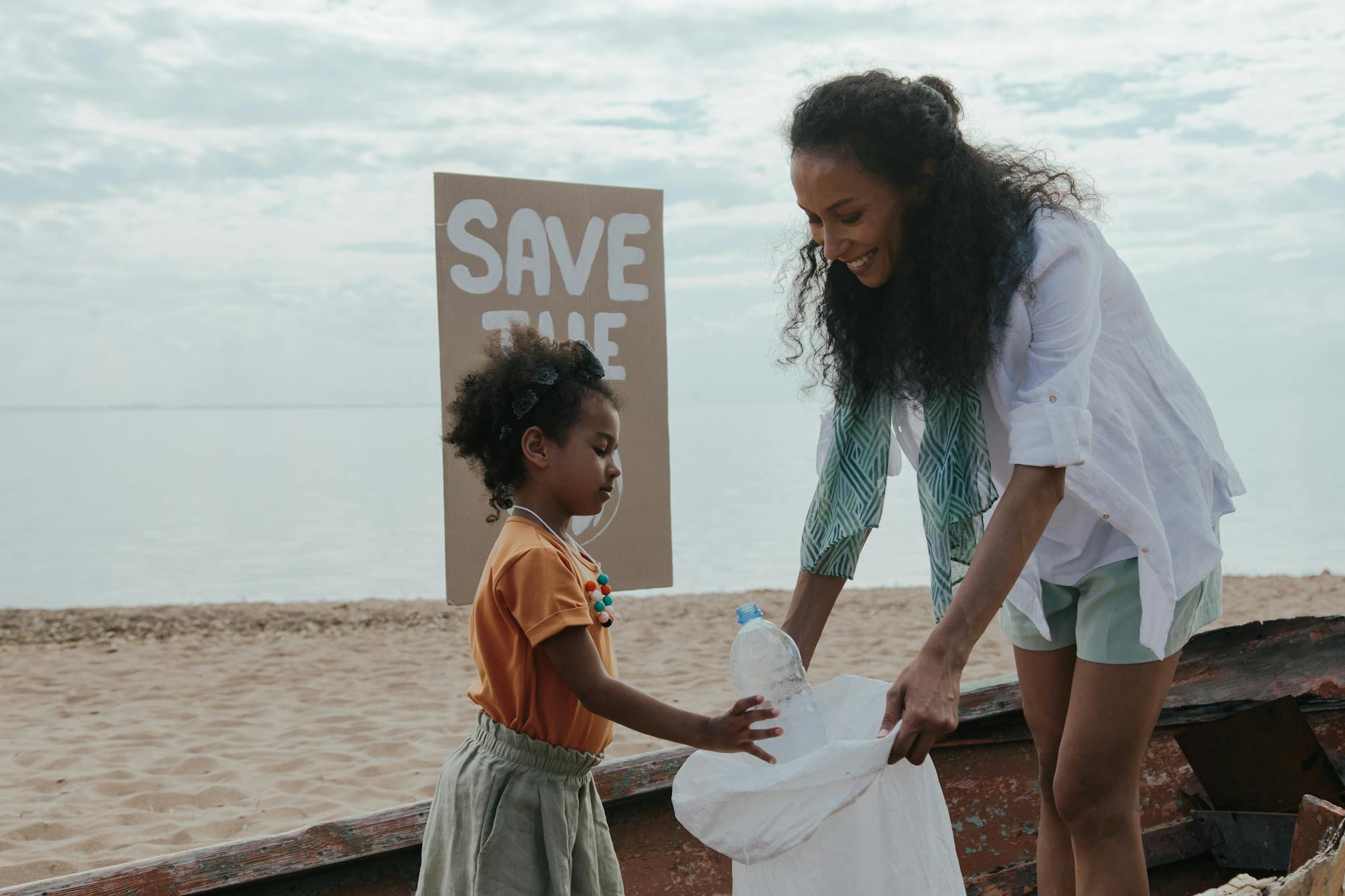 Mama z córką sprzątają plażę z hasłem Save the Ocean na tablicy
